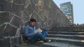 Ein Student liest auf der Treppe sitzend ein Buch.